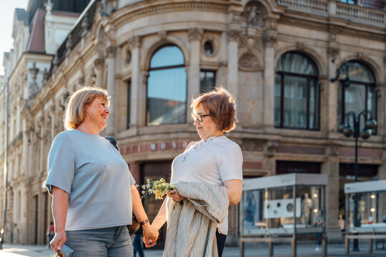 Happy Senior Female Friends Holding Hands While Walking Through Historic City Center Together