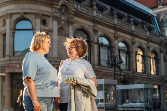 Happy Senior Female Friends Sharing Warm Conversation Near Historic European Architecture