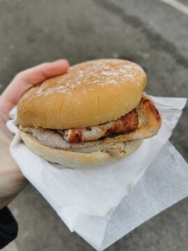 Close-up of a hand holding a freshly prepared bacon bap served in a white paper wrapper