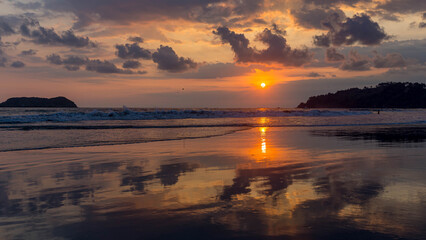 Obraz premium Vivid sunset over ocean waves reflecting on wet sand at tropical beach in Costa Rica