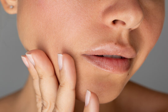 Young woman touching cheek with her fingers on a grey background. Close up of natural skin texture, pores, velvety softness and rosy complexion beauty concept