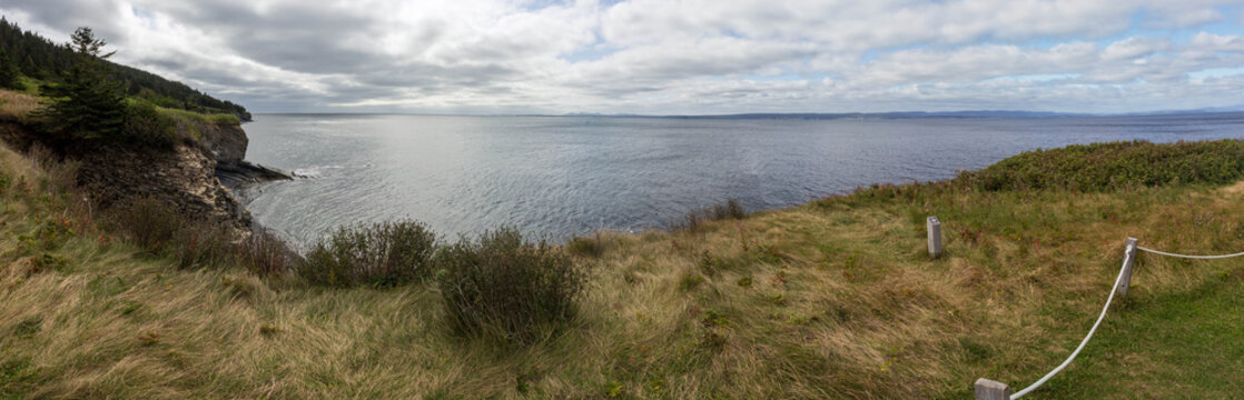 Panoramic coastal cliff view overlooking calm ocean bay under cloudy sky in Gaspesie
