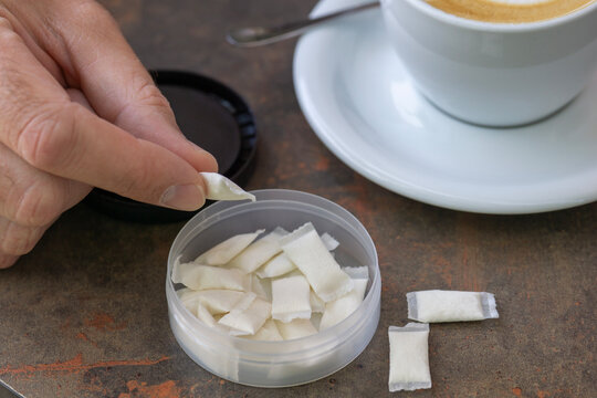 man holding white nicotine pouch or snus portion in fingers and a cup of coffee on a table in a cafe, person looking down at the pouch, casual modern lifestyle, alternative to smoking