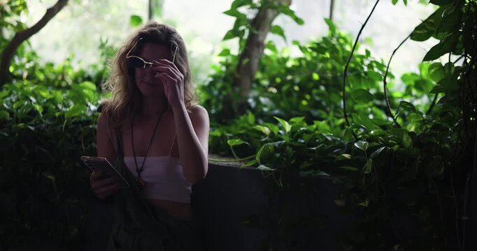 Young Woman Takes a Selfie and Smiles While Browsing Her Smartphone in a Serene Green Oasis, Enjoying a Relaxed Moment.