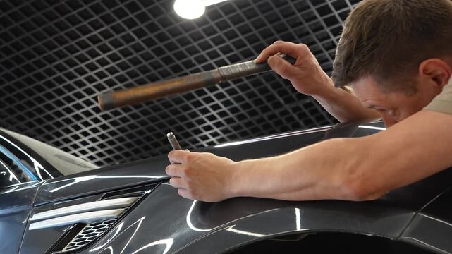 PDR. Paintless Car Dent Repair. Process of paintless dent repair on car body. The mechanic at the auto shop with tools to repair dents in car body. Body repair. A specialist repairs a dent on the car.