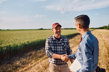 Happy mature farmer shaking hands with investment consultant in field. © Drazen