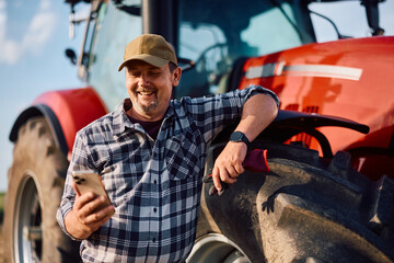 Happy farmer using smart phone by his tractor in field. © Drazen