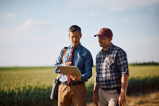 Insurance advisor using touchpad with farm owner in field.