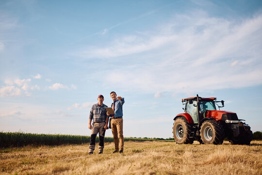 Full length of insurance advisor and farmer inspecting field.