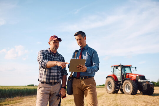 Mature farmer and insurance agent using digital tablet in field.