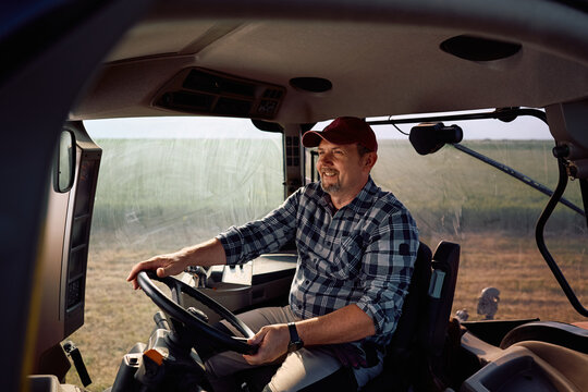 Happy agronomist driving tractor while working on farm.