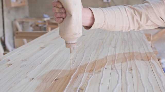 Carpenter applying glue to pine planks
