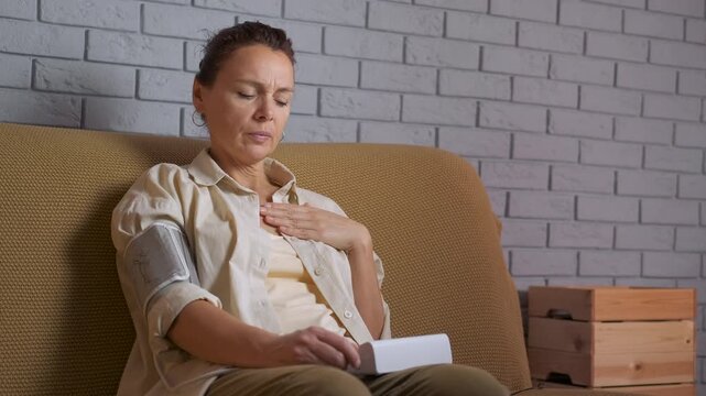 Woman measuring blood pressure suffering from chest pain. Unhealthy woman suffering from chest pain measuring her blood pressure with an electronic tonometer at home