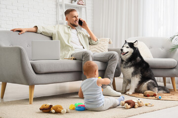 Modern father working remotely from home with laptop, talking on phone, baby playing, and pet husky dog © Pixel-Shot