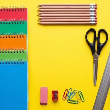 Colorful school and office supplies arranged as a frame on a bright yellow background with central copy space