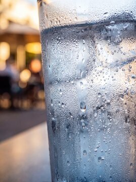 Close-up of a cold glass of water with ice cubes and condensation droplets against a blurred sunset background