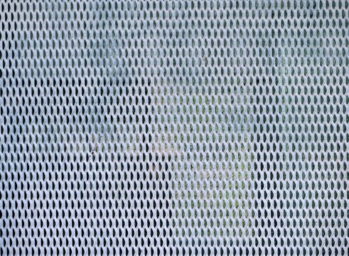  full-frame macro 
photograph of a white-painted, perforated 
metal mesh screen or grate. The screen 
features a dense, repeating pattern of small, 
diamond-shaped holes. The perspective looks 
throug