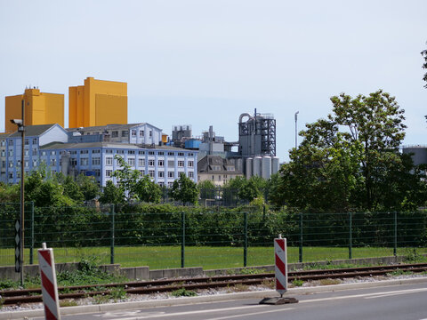  horizontal landscape shot 
looking over a multiple-lane paved road with a 
small concrete median and distant red-and
white safety bollards. Behind the road are 
railroad tracks running parallel to th