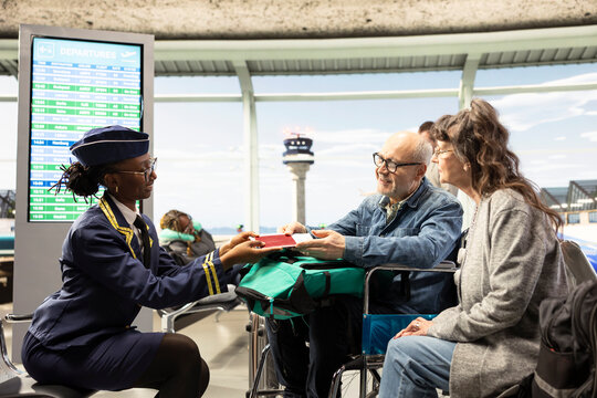 Flight attendant, cabin crew assisting passengers, wheelchair user and wife traveling during retirement, at airport terminal gate, accessibility and inclusion for reduced mobility, departure time.