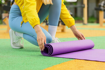 Naklejka premium Woman rolling up purple yoga mat after outdoor fitness workout, health and wellness lifestyle, this action represents the end of an exercise session and commitment to a healthy lifestyle