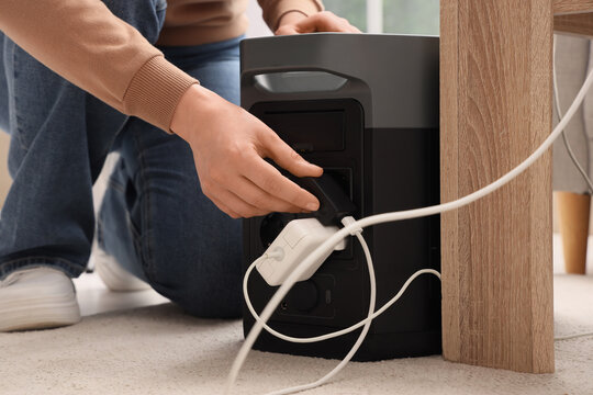 Person plugging charger into portable power station for device charging and emergency backup power, this modern technology offers convenient backup power for emergencies, outdoor activities