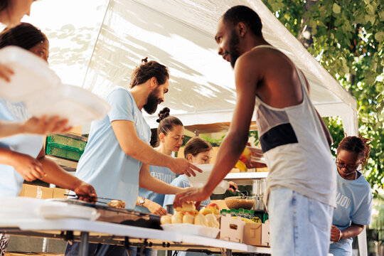 Multicultural team of charity workers serving food to refugees at outdoor nonprofit programme.