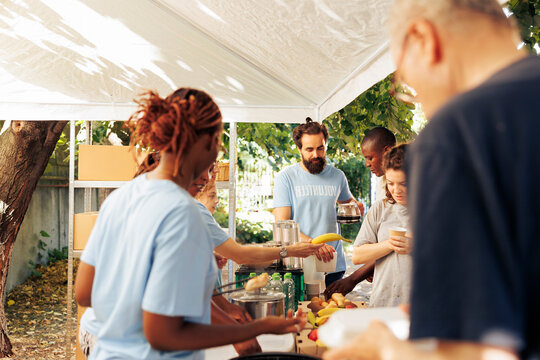 On sunny day, group of volunteers at local food bank handing out free food to the underprivileged homeless people outdoors, humanitarian aid team providing meals and non-perishable items to the needy.