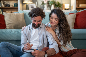 Young couple planning future together writing notes at home