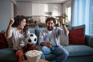 Naklejka premium Young couple celebrating sports victory watching soccer on tv
