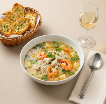 Crab soup with shrimp and rice, accompanied by garlic toast and a glass of white wine on a cloth table