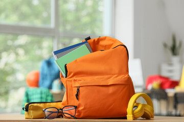 Orange backpack with school supplies, notebooks, glasses, and headphones on wooden table, back to school © Pixel-Shot