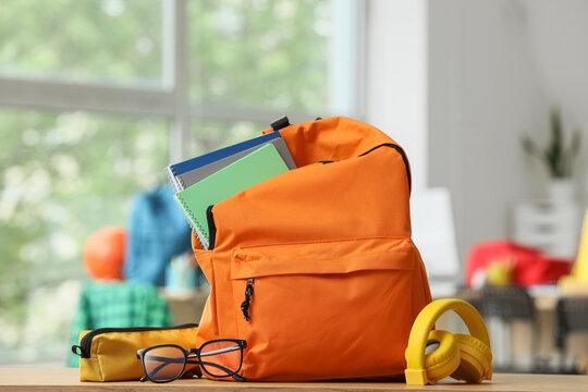 Orange backpack with school supplies, notebooks, glasses, and headphones on wooden table, back to school