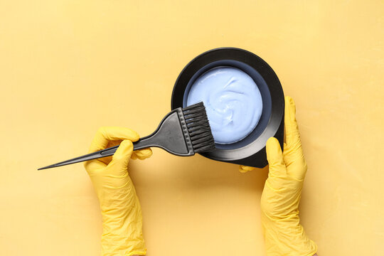 Hair dyeing process with blue bleach mixture in black bowl and applicator brush held by gloved hands, hair coloring and beauty treatment preparation