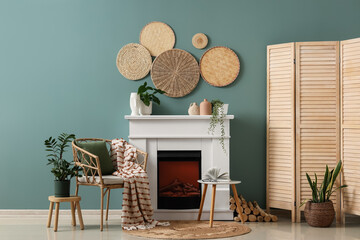Obraz premium Cozy living room interior with fireplace, wicker chair, houseplants, and decorative wall baskets on teal wall