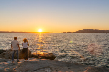 Fototapeta premium Couple standing on coastal granite rocks enjoying sunset views at Punta Tegge on La Maddalena island, Sardinia, Italy.
