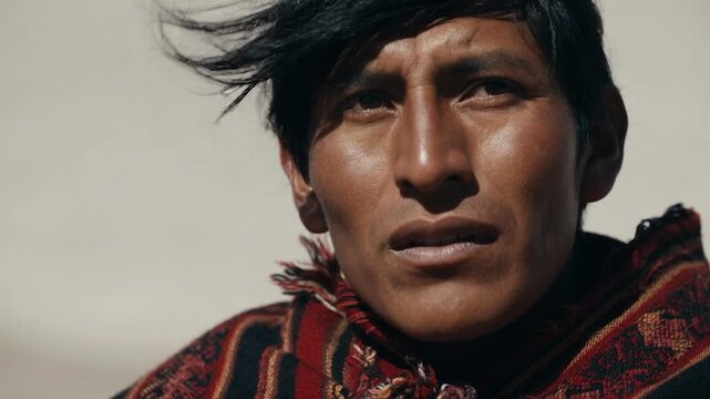 Indigenous peruvian man with windswept hair looking at the camera in the andes mountains with a serious expression