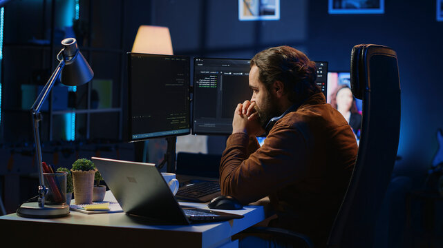 Technician focused on typing complex code in neon lit home office, developing software application. IT specialist removing headphones to better concentrate on difficult task, camera A.