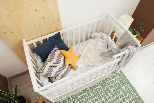 Cozy white baby crib with soft pillows and blankets in a modern nursery room, overhead view