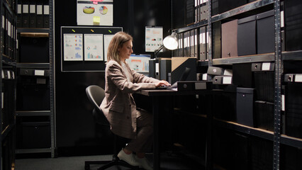 Investigator prepares to leave workplace with backpack after arranging documents. Female agent stands and goes out of evidence room after packing case files for investigation. Zoom-in shot. © DC Studio