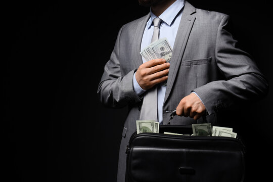 Businessman in gray suit hiding US dollar banknotes in jacket pocket and briefcase, financial corruption and illegal money