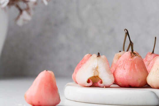 Light pink rose apples on a white marble tray, closeup view of rose wax apples on textured white background
