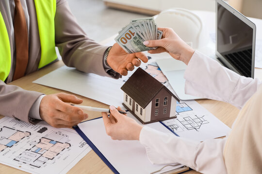 Real estate transaction with money exchange and house model on architectural plans, two individuals are engaged in a business agreement, with one person handing over cash to another