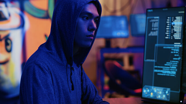 Asian hacker in dark hidden shelter trying to launch DDoS attack on website by sending large amounts of traffic from multiple sources to overwhelm IT. Evil computer scientists flooding target server.