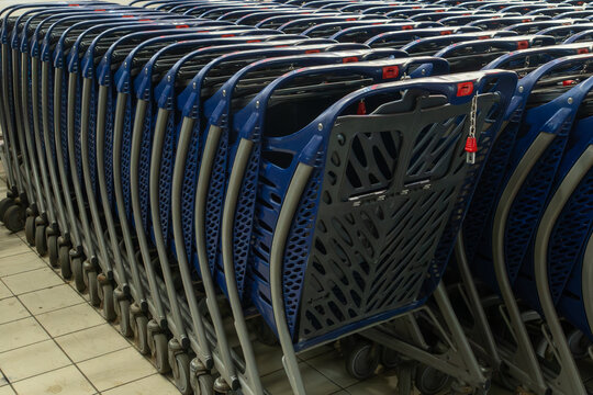 Neat rows of empty blue shopping carts stand in a supermarket terminal floor. This retail background is ideal for consumerism logistics and commercial grocery business marketing concepts.
