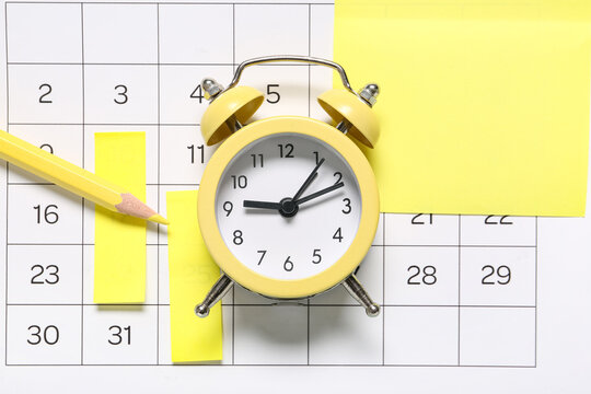 Yellow alarm clock, pencil, and sticky notes on calendar for time management and schedule planning