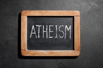 Atheism word written in white chalk on a small black chalkboard with wooden frame, philosophical © Pixel-Shot