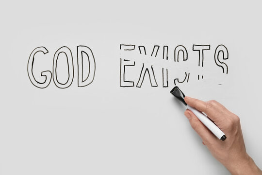 Hand erasing "god exists" text from whiteboard, atheism and belief concepts, religious doubt and questioning faith