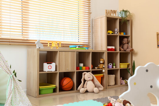Childrens playroom interior with wooden storage shelves, assorted toys, and bright window blinds