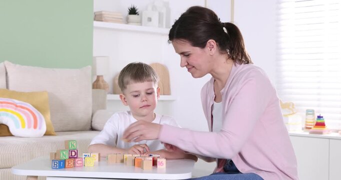 Mother teaching her son alphabet with letter cubes at table indoors