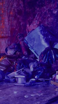 A collection of trash and waste sits against a brick wall in an urban location. The pile includes bags, containers, and metal objects. The scene shows the issue of litter in the city.